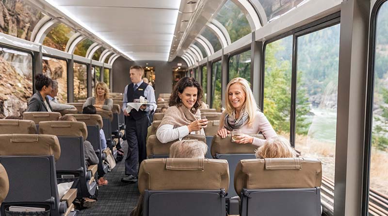 Two women chatting on a scenic train with mountain backdrop