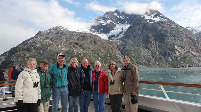 Group of friends posing on ship deck with snowcapped mountai