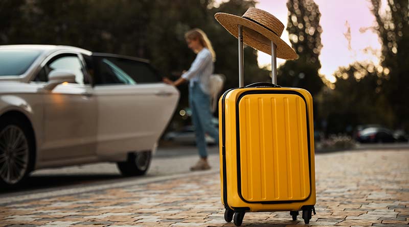 Yellow suitcase with hat woman entering car in background