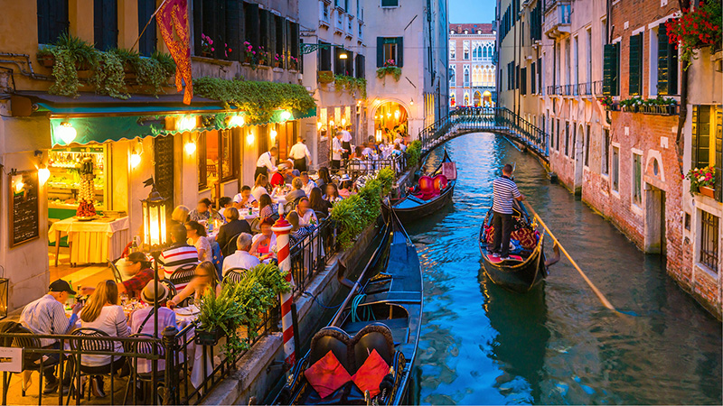 Gondolas in a Venice near people dining al fresco