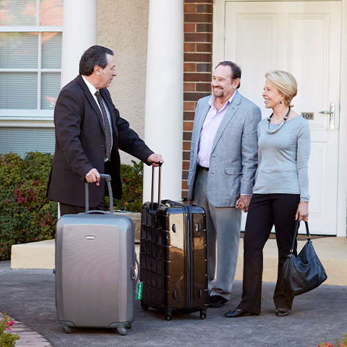 Driver picking up passengers with their luggage in front of home